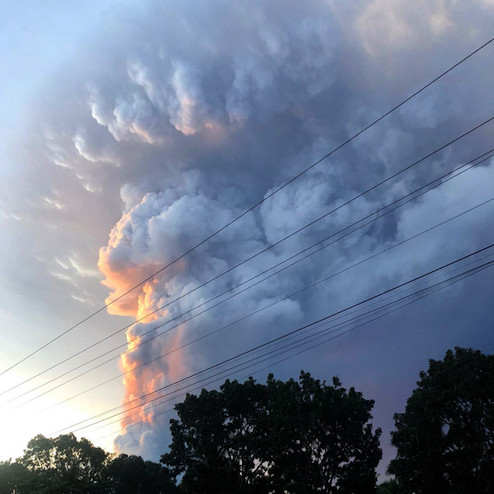 Huge plume of gray smoke in distant sky, lit from left by warm sunset light